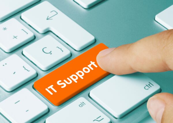 A finger presses an orange button on a white keyboard that says “IT Support”.