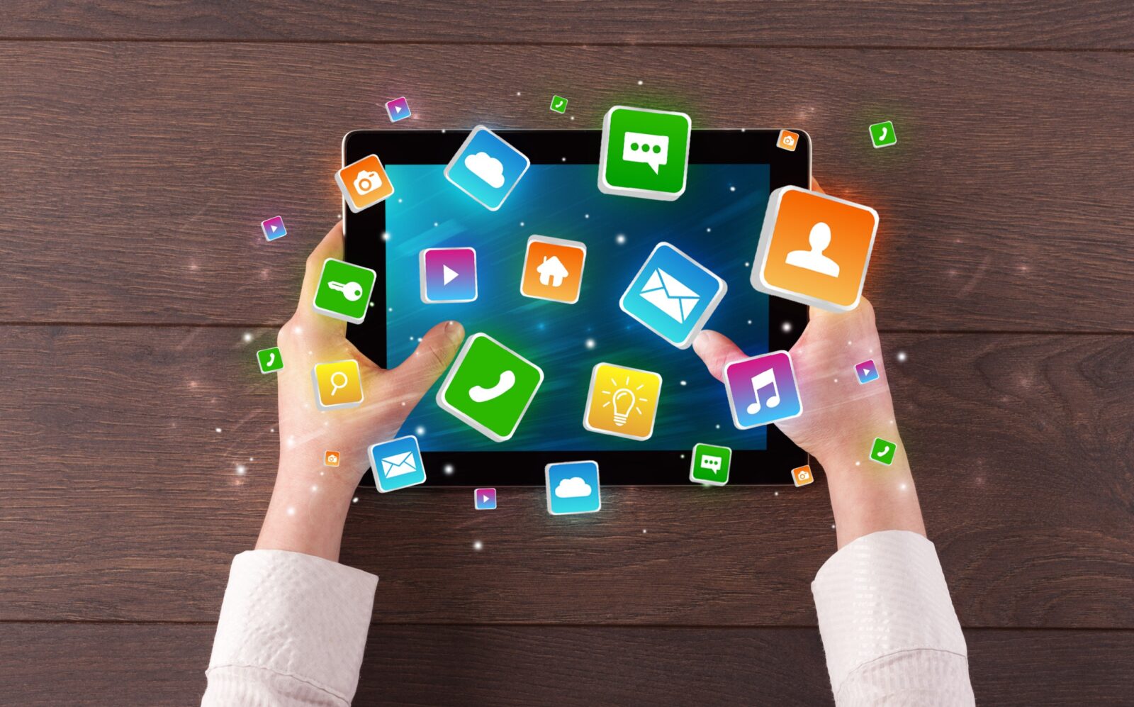 Man holding a tablet while colorful application symbols and icons bounce out of the screen.