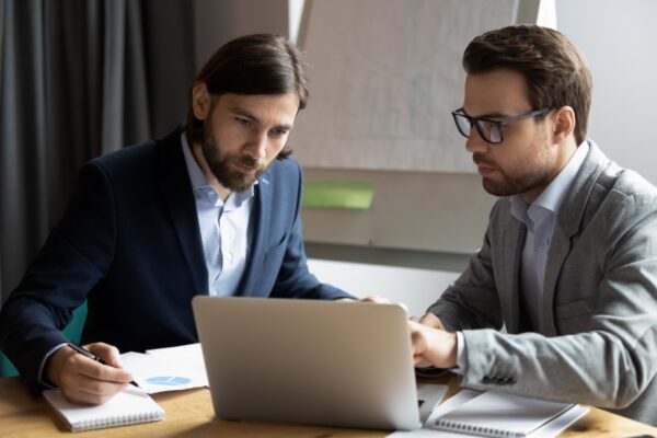 A business owner and IT specialist go over the report from a regular IT audit on a laptop.