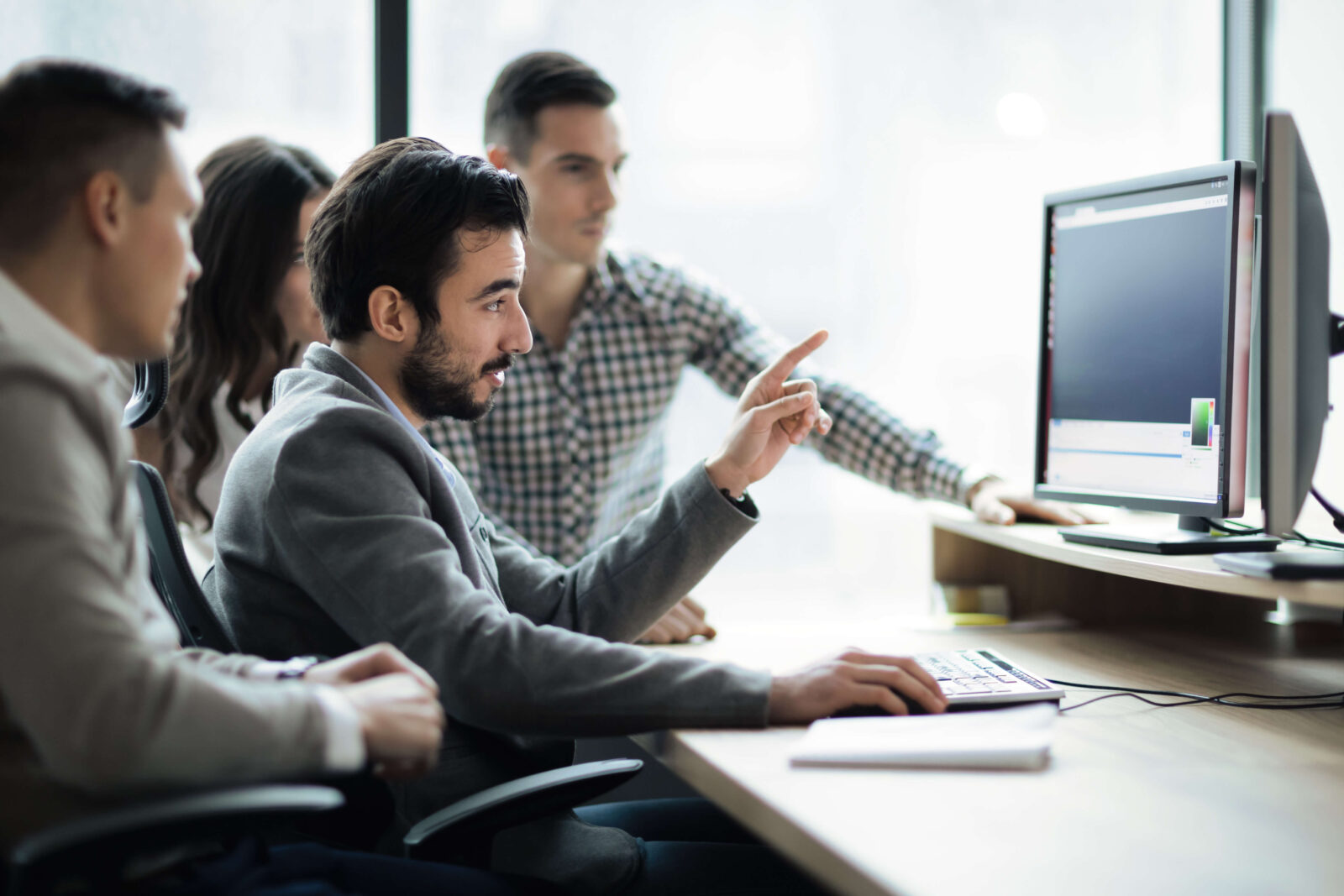 An IT consultant uses his desktop to explain a process to two men and a female sitting beside him.