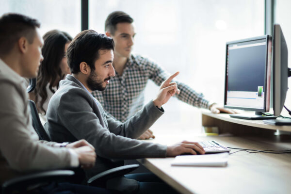 An IT consultant uses his desktop to explain a process to two men and a female sitting beside him.