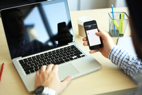 A man using a smartphone with a laptop placed in front of him, showcasing a BYOD setup in a modern workspace.
